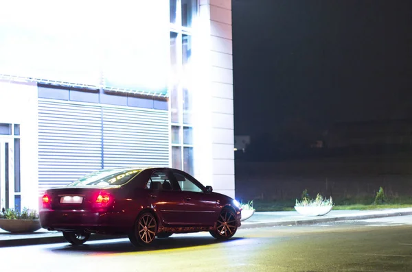 Kiraz kırmızı 4 kapılı aile d-sınıfı sedan Toyota Camry beşinci nesil xv30 2001-2006 led farlar ve 18 inç jantlar büyük jantlar ile yaz bir arka plan üzerinde yeşil bir alan ve orman üzerinde ayakta