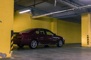 Vişne kırmızısı 4 kapılı yeraltı otoparkı D sınıfı sedan Toyota Camry beşinci nesil XV30 2001-2006 gri bir tarlada duruyor ve arka planda sarı duvarlar kurşun farları ve 16 inç jantları var. 