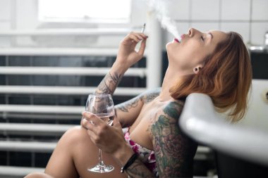 Renkli dövmeler ile yaramaz kız beyaz banyo üzerinde eğilir