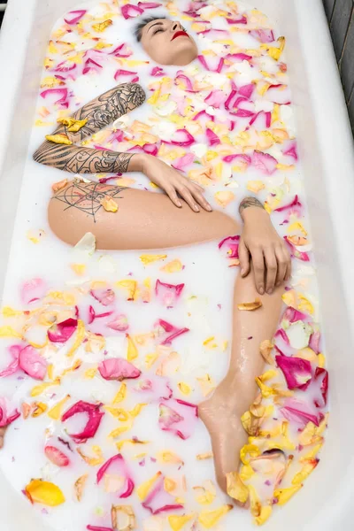 Charmig tjej med snygga tatueringar ligger i vit badet full av — Stockfoto