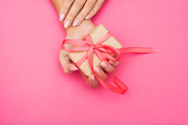 Mãos de mulher segurando caixa presente com uma fita em fundo rosa pastel  . — Fotografia de Stock