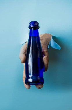 Bir el yırtık bir kağıttan mavi bir su şişesini tutar..