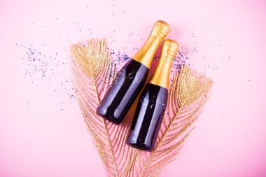 Kutlamanın düzleşmesi. Pembe arka planda renkli parti flamaları olan şampanya şişesi..