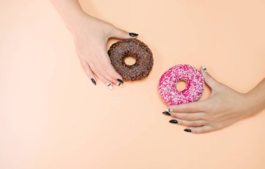 Renkli arka planda kremalı iştah açıcı çörekler ve güzel manikürlü kadın elleri..