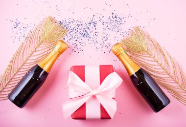 Kutlamanın düzleşmesi. Pembe arka planda renkli parti flamaları olan şampanya şişesi..