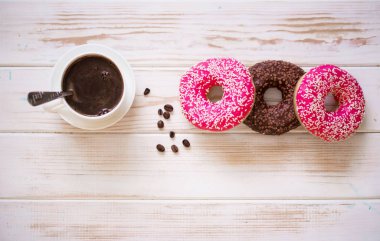 Pembe kremalı lezzetli çörekler ve beyaz ahşap arka planda bir fincan aromalı kahve..