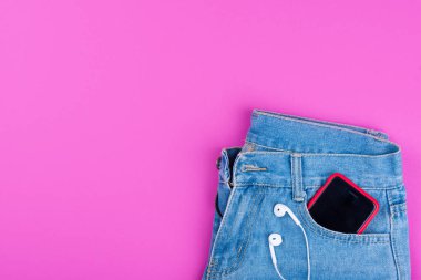 Mavi kot, arka cebinde pembe arka planda müzik için kulaklıklı bir telefon..