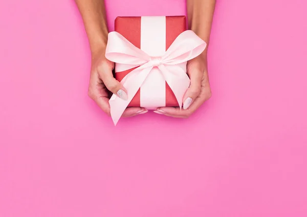 Mãos de mulher segurando caixa presente com uma fita em fundo rosa pastel  . — Fotografia de Stock