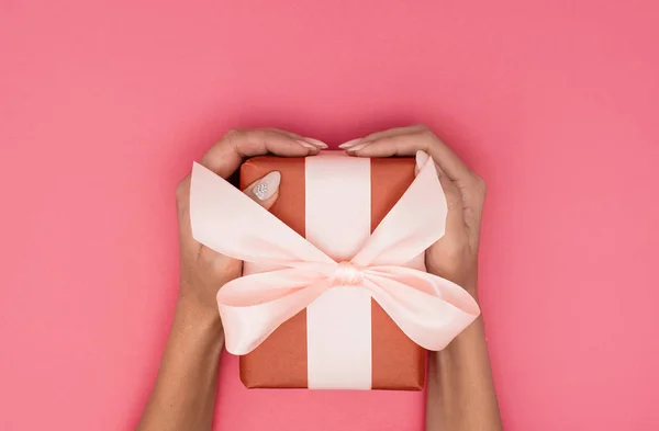 Frau Hände halten Geschenkbox mit einem Band auf pastellrosa Hintergrund . — Stockfoto