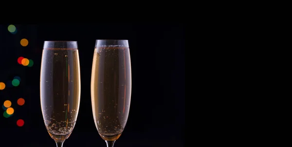 Két pohár pezsgővel, ünnepi fényekkel, sötét háttérrel.. — Stock Fotó
