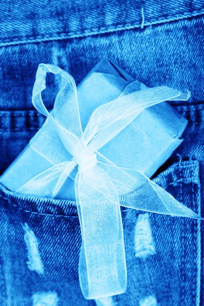 Ein kleines Geschenk in Bastelpapier und ein goldenes Band in einer Tasche aus blauer Jeans. — Stockfoto