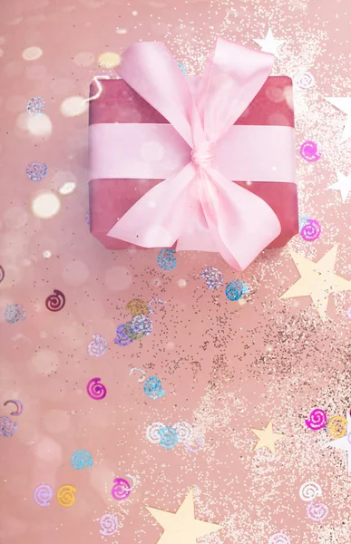 Hermosa caja de regalo con cinta de satén en colores delicados y destellos sobre un fondo rosa . —  Fotos de Stock