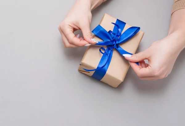 Gri bir arka planda elinde hediyeyle şık bir kadın manikürü..