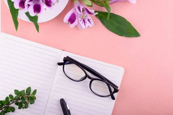 흰색 컵, 아름다운 꽃, 분홍색 배경, 펜과 안경이있는 노트북의 향기로운 차. — 스톡 사진