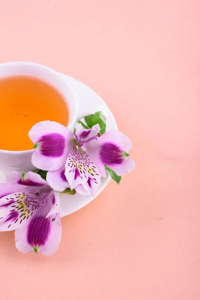 Lindas flores de astromeria. Chá de ervas em uma xícara branca e um pires branco em um fundo rosa — Fotografia de Stock