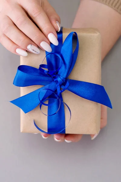 Bella manicure femminile elegante su uno sfondo grigio con regalo in mano . — Foto Stock