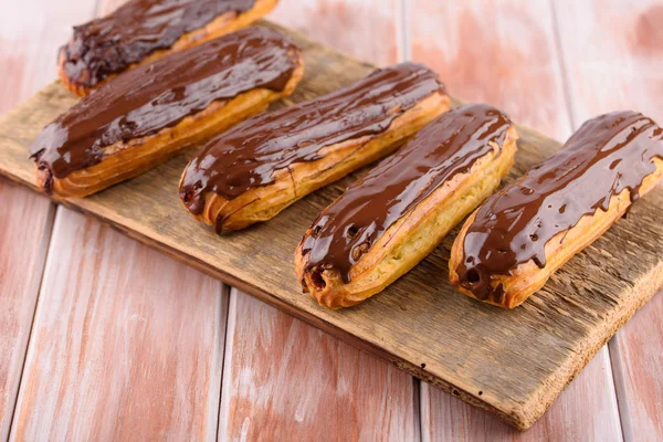Ahşap bir tahta üzerinde çikolata ile lezzetli ve güzel eclairs. Iştah açıcı bir tatlı. Parti malzemeleri