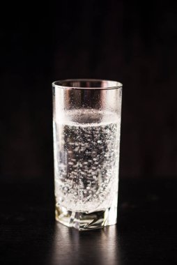 Siyah bir masa ve siyah arka planda, bir bardakta gaz verilmiş su..