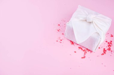 Güzel küçük güller, küçük kalpler, sütlü çikolatalar, pembe arka planda beyaz renkli güzel bir Furoshik armağanı..