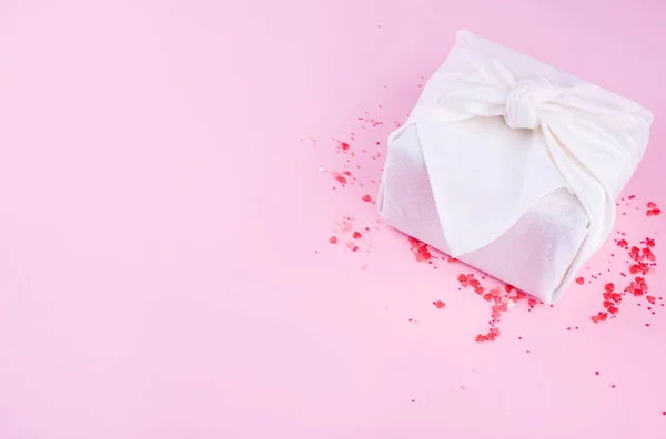Девчонки, маленькие сердца, сердца молочного шоколада, на розовом фоне с красивым подарком фурошика белого цвета . — стоковое фото