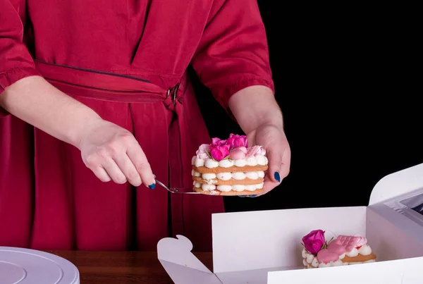 The hands of the confectioner with a delicate and delicious cake of letters. Cake with live flowers, white chocolate, beas. Hands of a pastry chef, packing dessert. — Stock Photo, Image