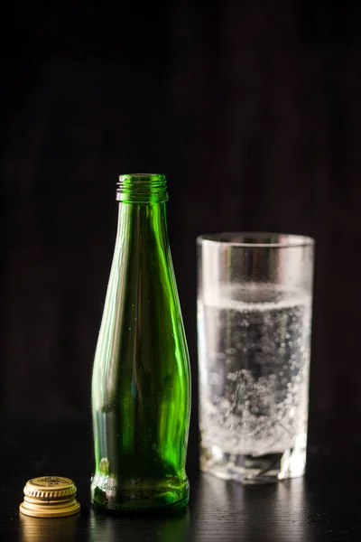 Минеральная вода в высоком бокале. Темный фон с бутылкой и стаканом воды . — стоковое фото