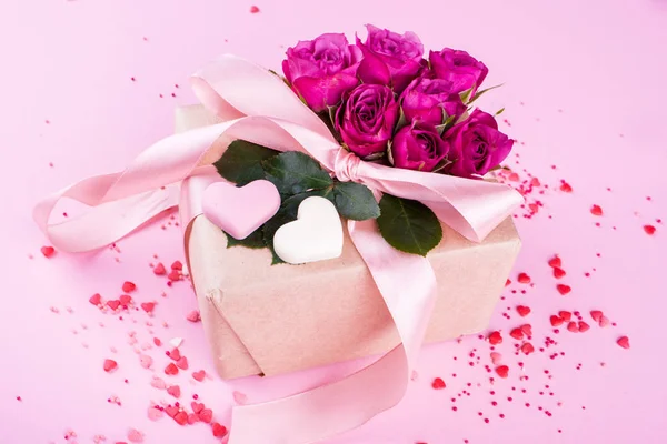 Presente com fita de cetim com pequenas rosas em um fundo rosa. Corações, conteúdo festivo. Dia dos Namorados . — Fotografia de Stock