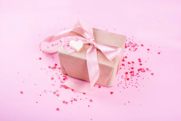 Gift with satin ribbon with small roses on a pink background. Hearts, festive content. Valentine\'s Day.