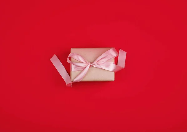 Sebuah hadiah yang indah dengan pita satin warna merah muda lembut, dengan latar belakang merah cerah . — Stok Foto