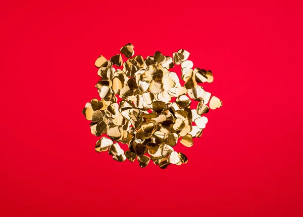 Dulces de oro en forma de corazones pequeños sobre un fondo rojo brillante . — Foto de Stock