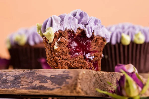 초코 렛 컵 케익 이 나무 식탁에 놓여 있고, 안 에는 과일 잼이 들어 있는크 리마 꽃이 들어 있다. — 스톡 사진