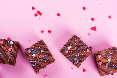 Chocolate brownie dessert with almonds inside, festive powder, on a pink background.