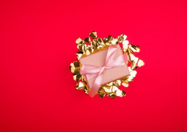 Saten pembe kurdeleli güzel bir hediye kutusu, kırmızı bir bckground üzerinde altın konfeti.