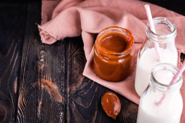 İki şişe taze süt ve siyah arka planda ev yapımı tuzlu karamel. Nefis kahvaltı.
