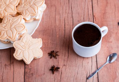 Çiçek şeklinde kremalı kurabiyeler, hafif ahşap arka planda. Güzel kokulu kahve.