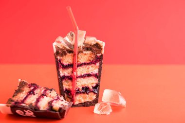 Tatlı olarak bir bardak buzlu içecek ve kırmızı arka planda bir tüp. Karamel, pasta, krema, çikolata.