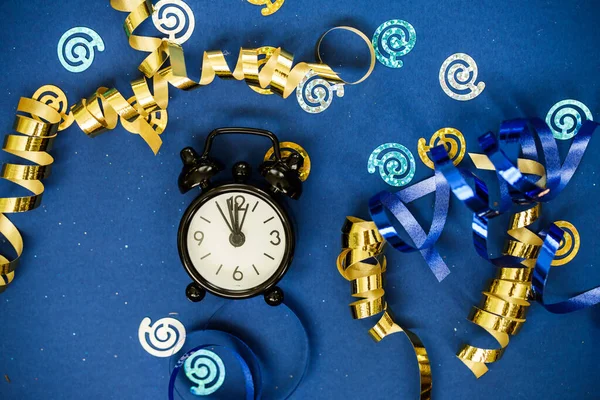 Black clock alarm clock among gold osperpantin, sequins on a blue background. Holiday content.