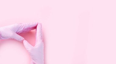 Tıbbi eldivenli eller pembe renktedir. Pembe arka planda kalp şeklinde ve mesaj için bir yer vardır..
