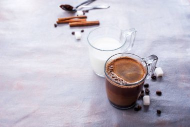 Lezzetli ve mis kokulu kahve, bir bardak süt, kokulu tarçın çubukları, kahve çekirdekleri, şeker küpleri masaya.