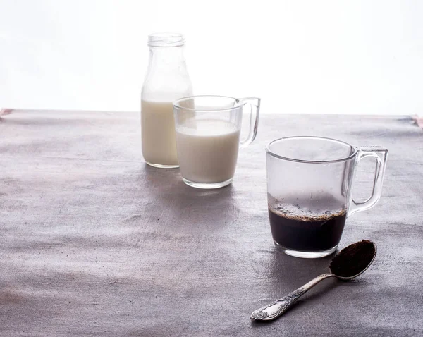 Cervejando café em uma xícara de vidro, um jato de água quente, leite em uma garrafa, uma colher com café creme — Fotografia de Stock