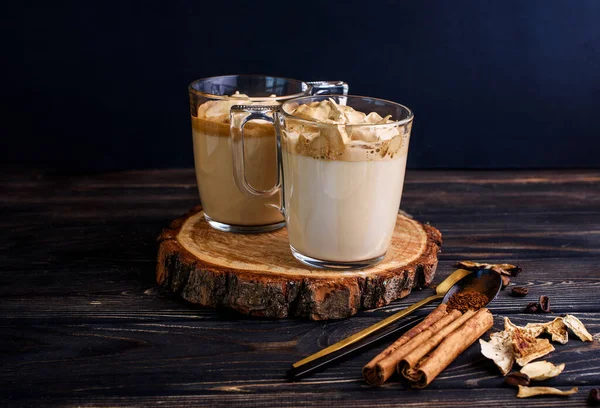 Delizioso e profumato caffè dalgona in tazze di vetro, bastoncini di cannella, funghi secchi, un cucchiaio di caffè istantaneo, zucchero . — Foto Stock
