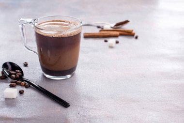 Lezzetli ve mis kokulu kahve, bir bardak süt, kokulu tarçın çubukları, kahve çekirdekleri, şeker küpleri, masada.