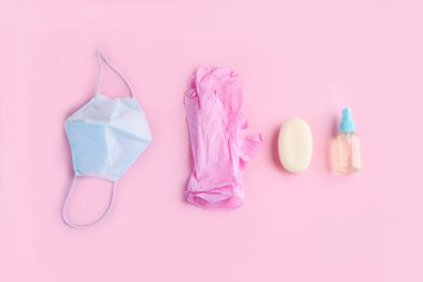 Mavi yüz maskesi, pembe eldivenler ve pembe arka planda el aptiği yalanı. Virüsten korunma