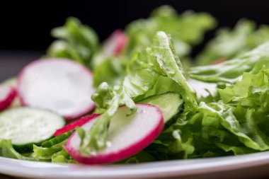 Taze ve lezzetli salata, marul, turp, salatalık ve zeytinyağı beyaz bir kasede, masada sunulan adaklarla.