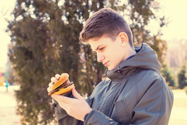 Τρώγοντας ένα cheeseburger σχετικά με τη φύση ο νεαρός άντρας — Φωτογραφία Αρχείου