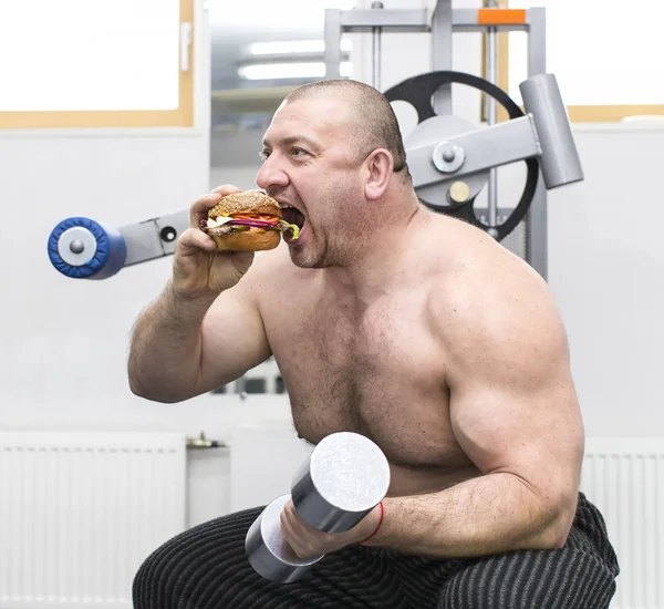 Adam bir hamburger et ve peynir ile spor salonunda yiyor. — Stok fotoğraf