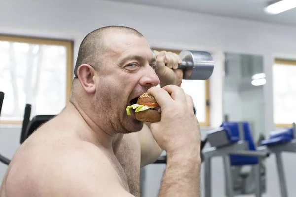 Man eats a hamburger with meat and cheese in the gym Royalty Free Stock Images