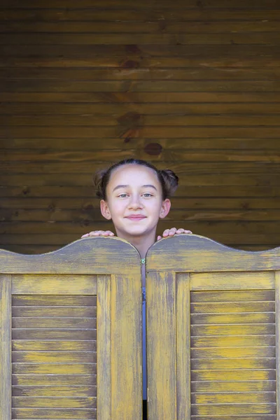 Girl looks out from behind  wooden door — Stock Photo, Image