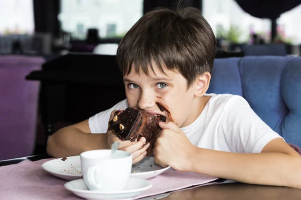 El chico se está comiendo un pedazo grande de pastel. —  Fotos de Stock