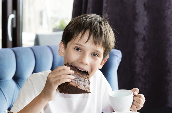 O menino está comendo uma grande fatia de bolo — Fotografia de Stock